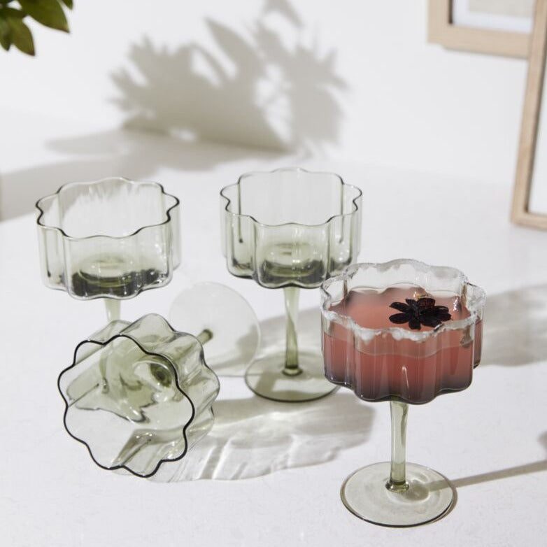 4 Sonnet Smoky Green Modern Floral Shaped Coupe Glasses Staged, One tipped over, One filled with a berry pink cocktail.