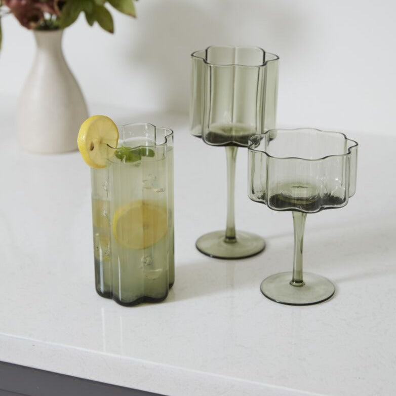 Sonnet Smoky Green Glass Drinkware Collection Highball Glass filled with Lemon Cocktail next to Wine glass, Coupe glass