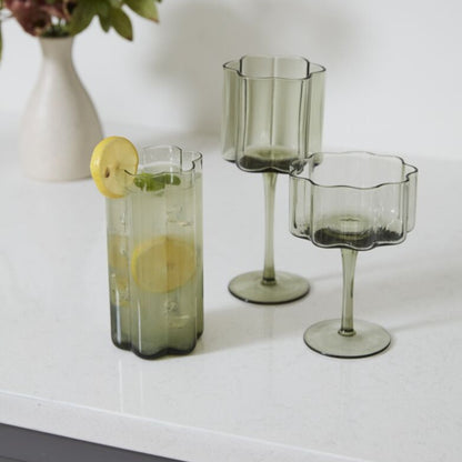 Sonnet Smoky Green Glass Drinkware Collection, Highball glass filled with lemon cocktail, Wine glass, and Coupe Glass