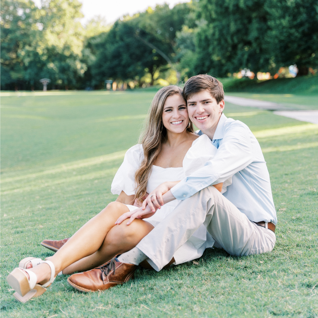 Woman in White Puff Sleeve Dress and Man in Light Blue Dress Shirt and Khaki Pants sitting in Green Grass