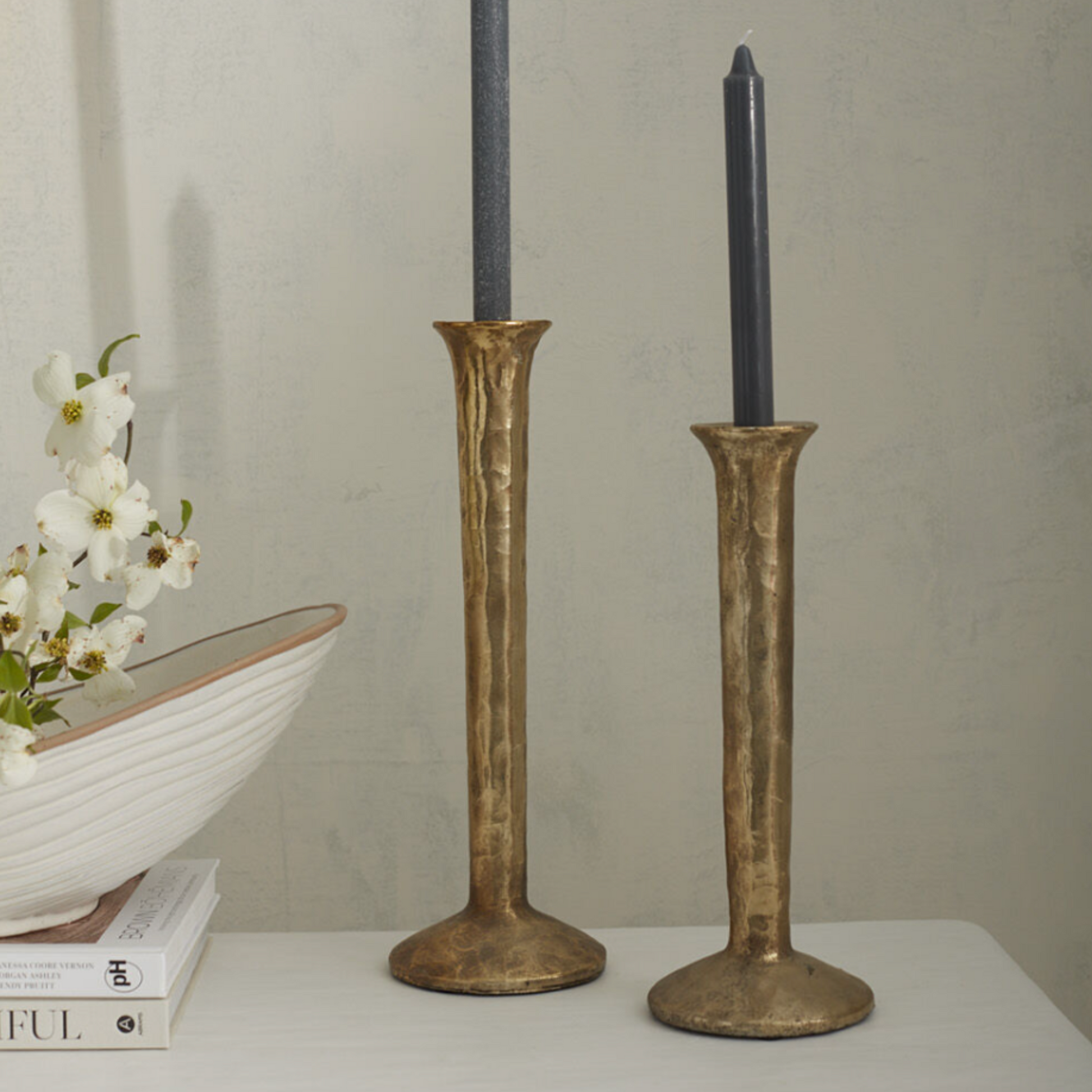 Athena Taper Holder in two sizes with a spool-shaped metal design, topped with a mottled gold finish, exuding an aged and organic charm styled with blue taper candles.