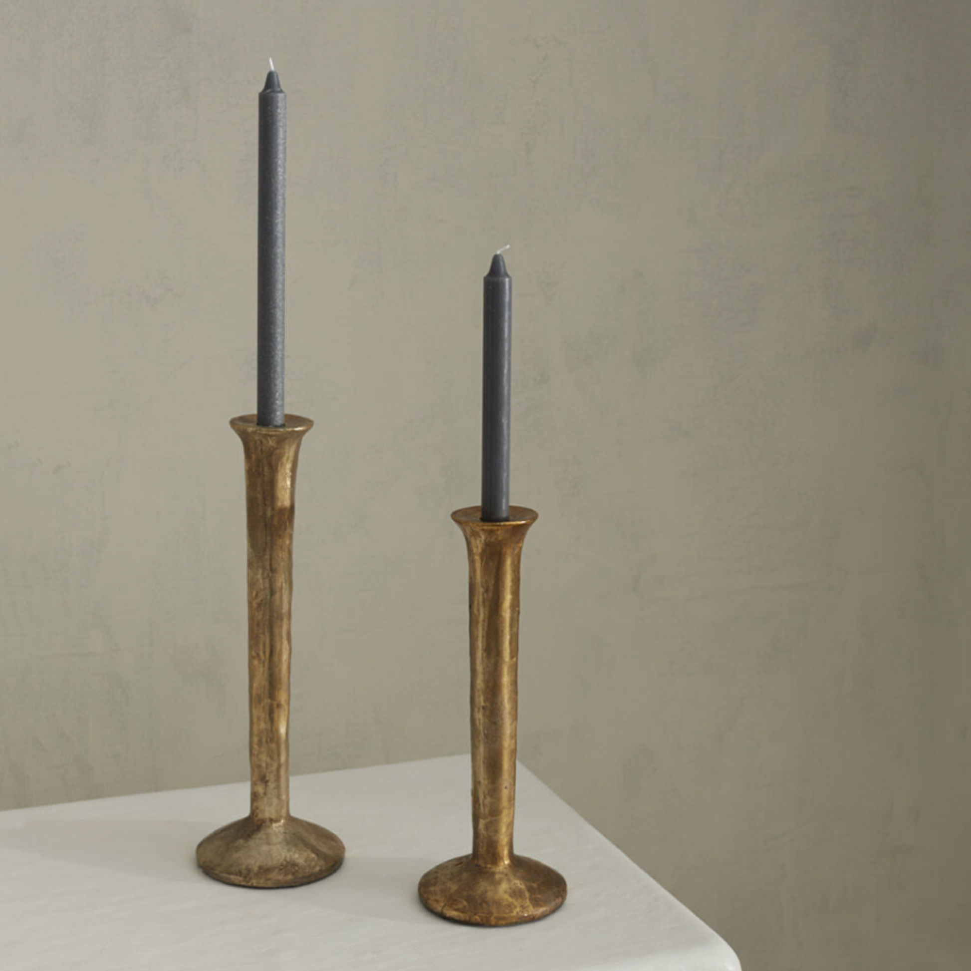 Athena Taper Holder in two sizes with a spool-shaped metal design, topped with a mottled gold finish, exuding an aged and organic charm, styled with blue taper candles.