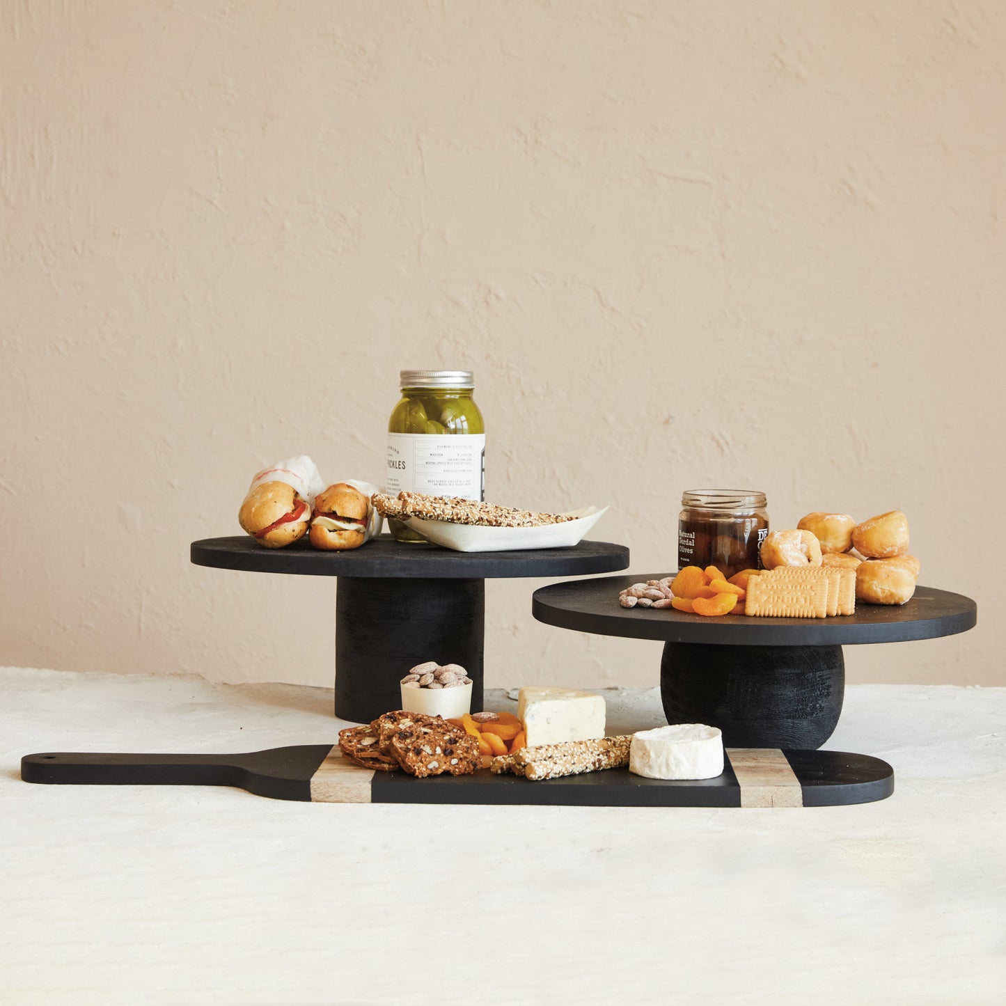 Calder Black Finished Modern Mango Wood Pedestal with Rounded Base, Short and Tall styled with Sandwiches, Cheeses, and Crackers