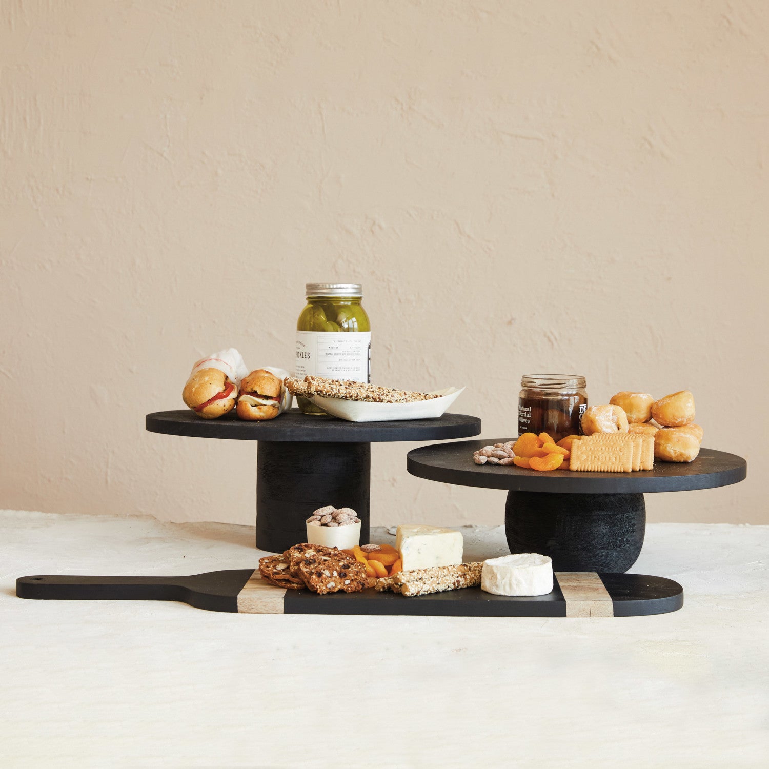 Calder Black Finished Modern Mango Wood Pedestal with Rounded Base, Short and Tall styled with Sandwiches, Cheeses, and Crackers