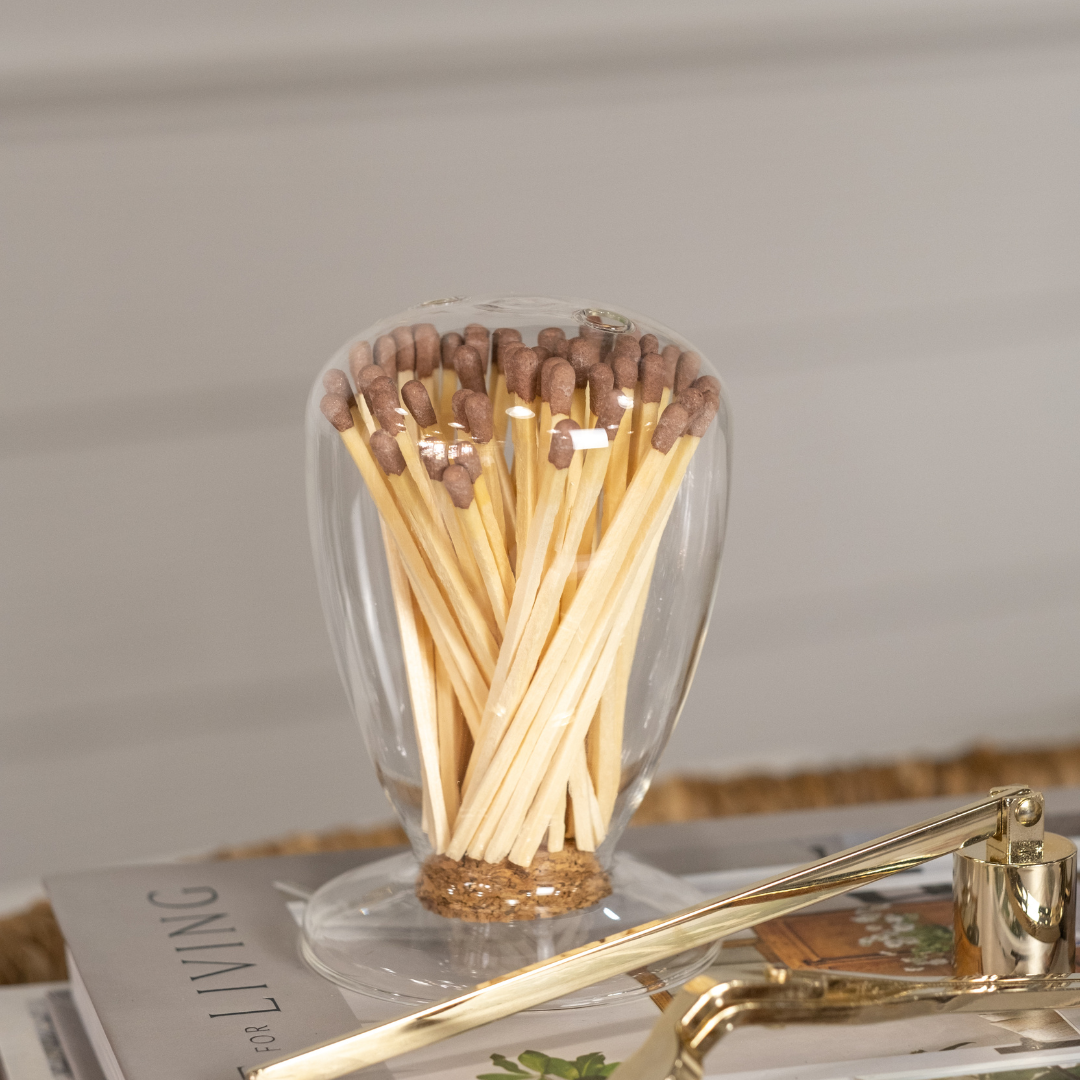 Simple Minimalist Glass Match Cloche with Top Match Dispensing Holes and Striker on Cork Stopper displayed with pink tip matches, gold wick trimmer and candle snuffer