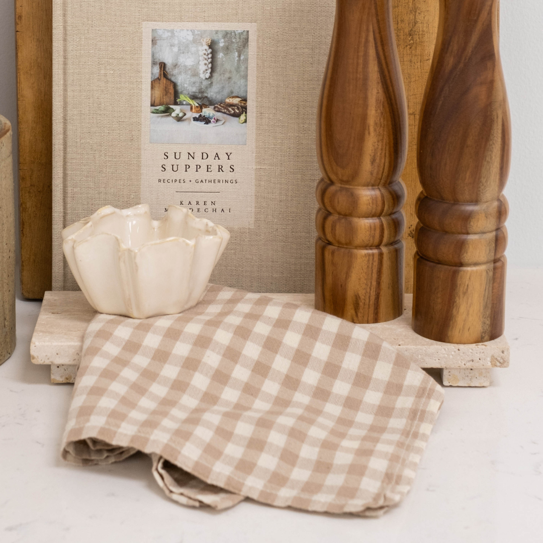 Footed Greige Travertine Serving Board or Decorative Display Piece Styled with Cookbook, Dish, and Gingham Tea Towel